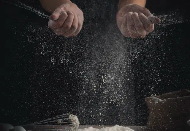 Flour poured on a table beside eggs and a whisk for bakery kitchen