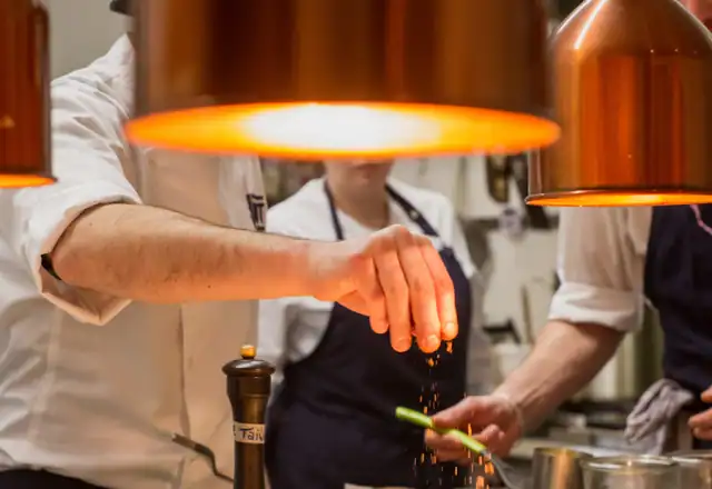 Chef seasoning food under warm copper lamps for cleaning vs sanitizing equipment