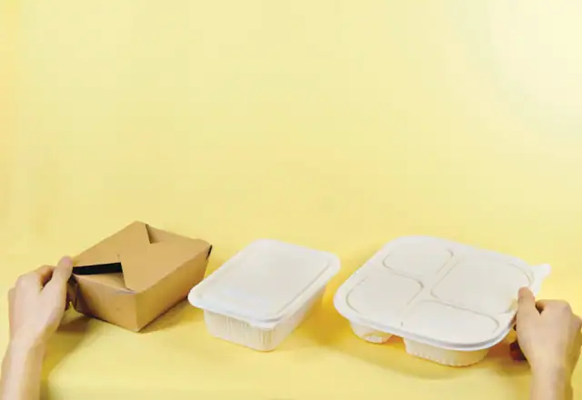 Person holding a box and two takeout containers for central production kitchen rental