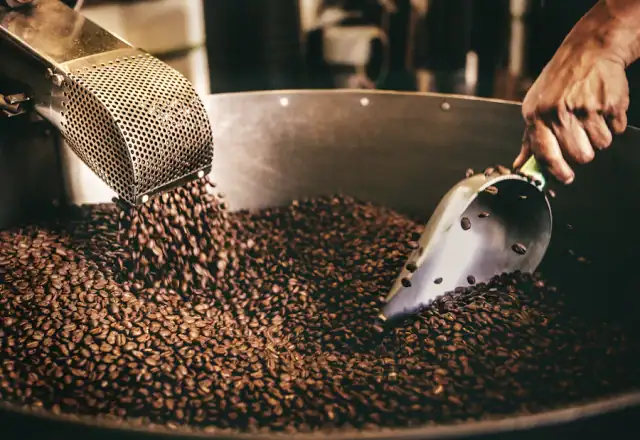Metal scoop stirring roasted coffee beans for batch coding and product traceability