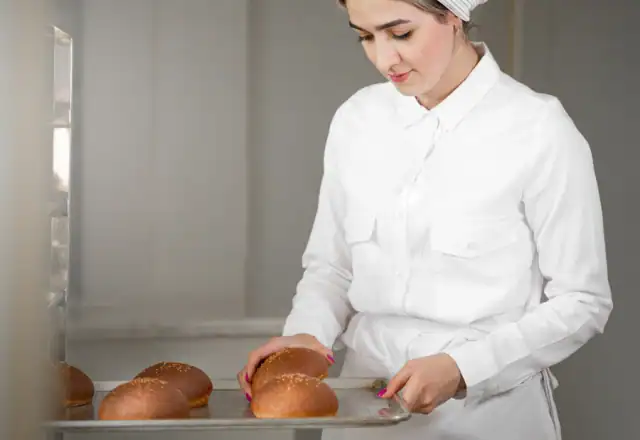 Baker placing fresh bread rolls on a tray for ovens and baking equipment
