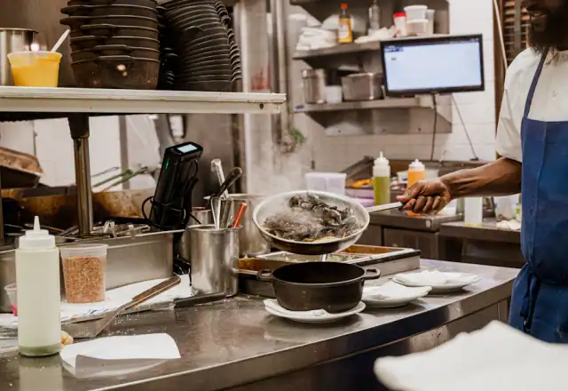 Cook preparing food at a station in a commercial kitchen for designing a menu for efficient production