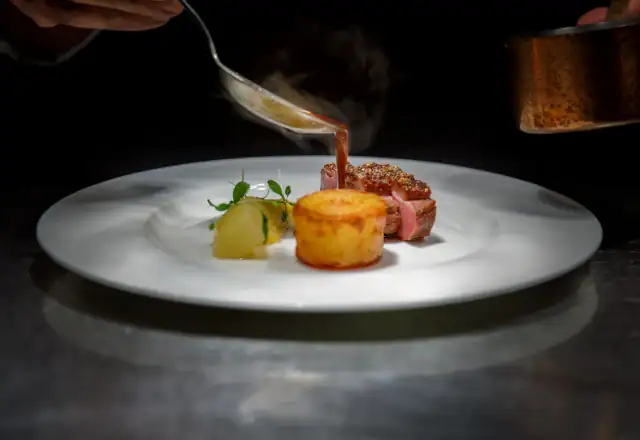 Chef pouring sauce over a plated steak for designing a menu for efficient production