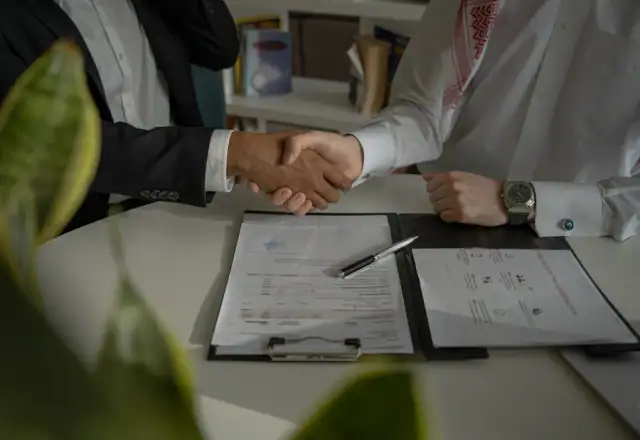 Two people shaking hands over a document for request a rental quote