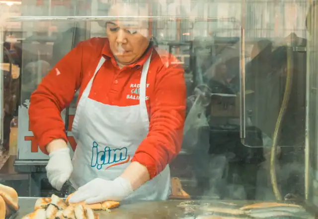 Cook preparing food behind a glass counter for food packaging area