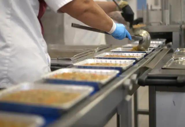Worker filling food trays on a conveyor belt for availability and booking