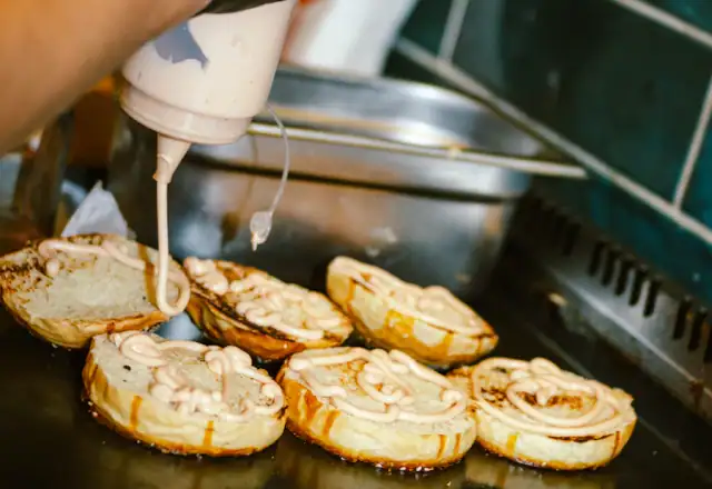 Gloved hands squeezing sauce onto toasted buns for starting a packaged food brand