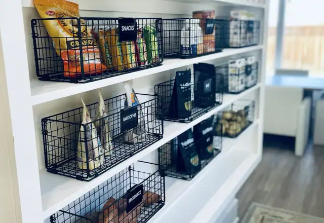 Black wire baskets on white shelves holding snacks for dry ingredient and packaging storage