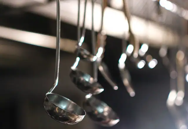 Metal ladles hanging from a rack in a professional kitchen for designing a menu for efficient production