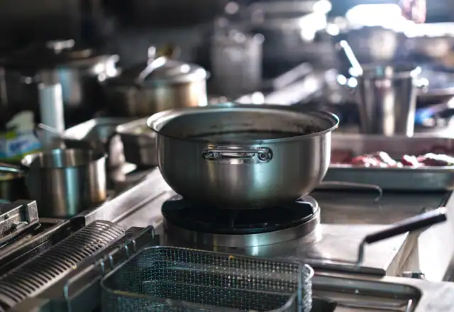 Stainless steel pots and a deep fryer basket on a commercial range for kitchen rules and hygiene